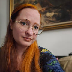 Photograph of a woman with two-tonented hair and round gold glasses.
